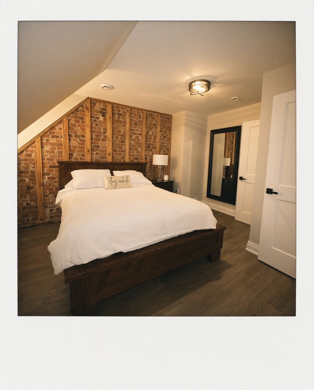 Upstairs bedroom at 763 Monmouth Road with an exposed brick accent wall under the sloped ceiling, walnut bed frame and full-length mirror
